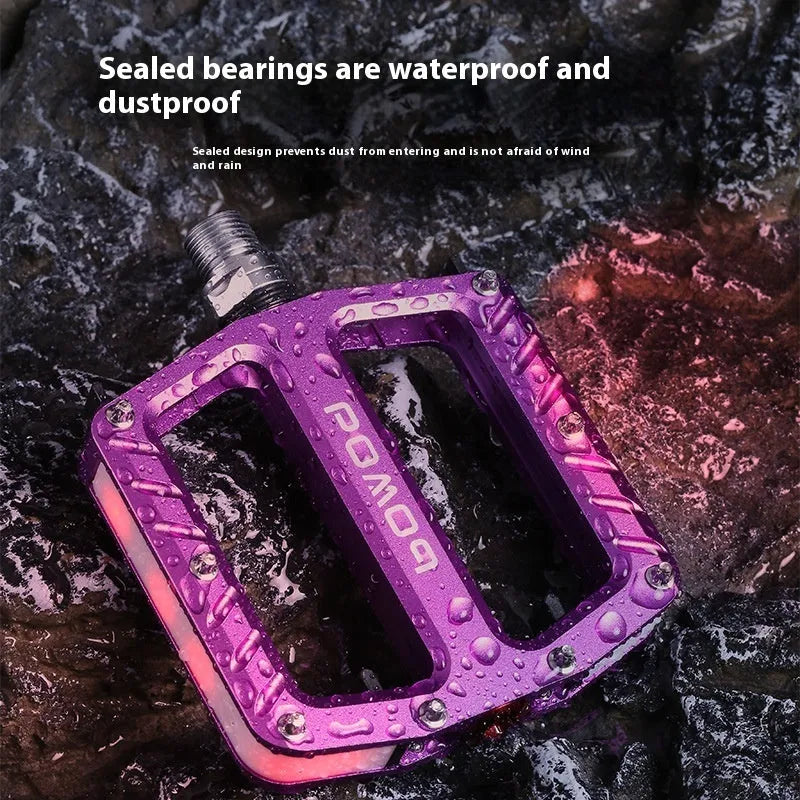 Aluminium alloy bicycle pedals with built-in LED lights in purple, black, titanium, red, and gold colour options.