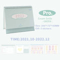 Coil bound paper desk calendar in green on a desk, regular size 100mm x 100mm x 172mm