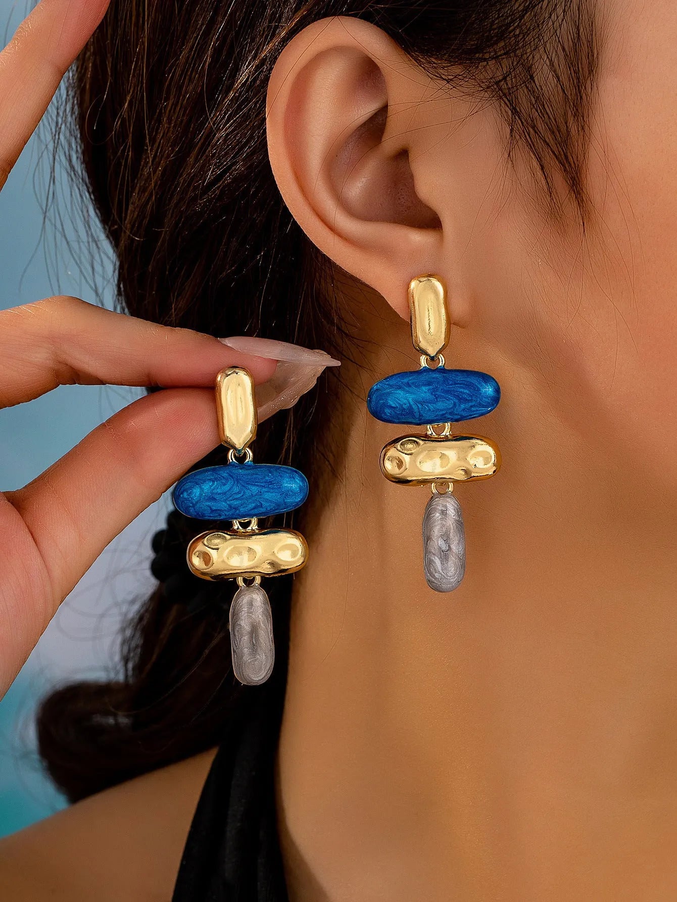 A pair of geometric-shaped stud earrings with a multicolour metallic finish on a plain background.