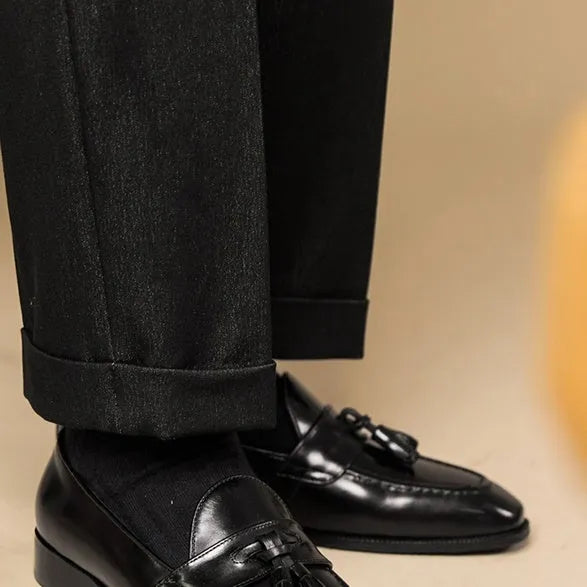 Men's black genuine leather tassel loafers on a solid background, showing polished upper and rubber sole.