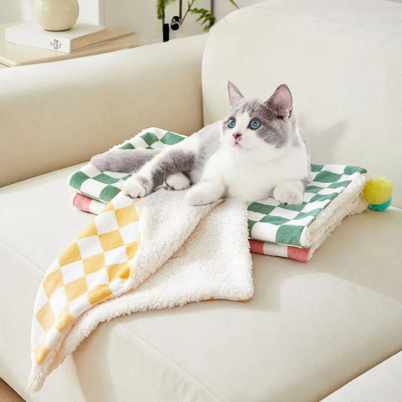 Green plaid pattern soft fleece pet blanket with fur ball decoration on a sofa