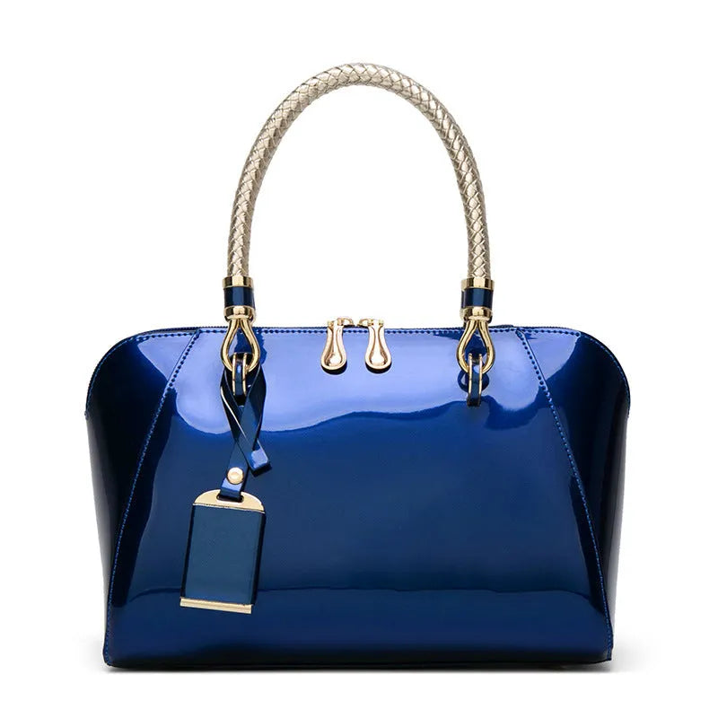 Shiny blue PVC patent leather handbag with lock closure and crossbody strap on a white background