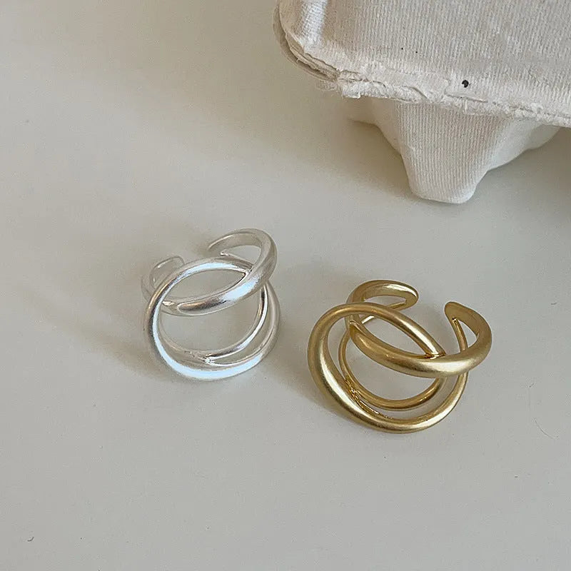 Geometric open ring for women with a 3D interlaced design in matte metal, shown in gold and silver finishes.