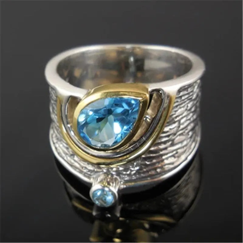 Blue zircon drop-shaped ring with Chinese style rhinestone inlay, shown on a finger.