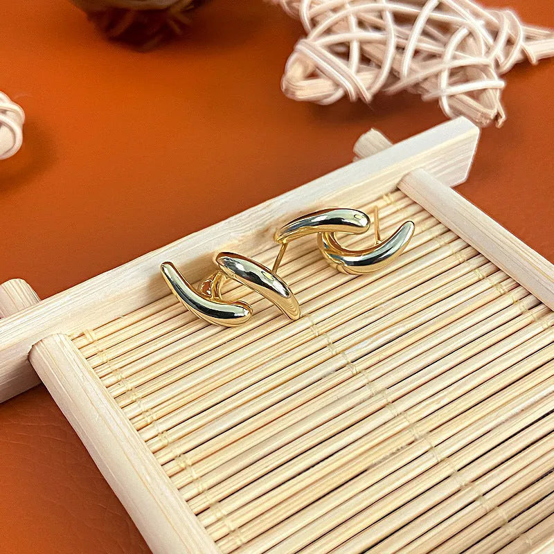 Women's textured line geometric copper stud earrings in silver and gold tones on neutral background