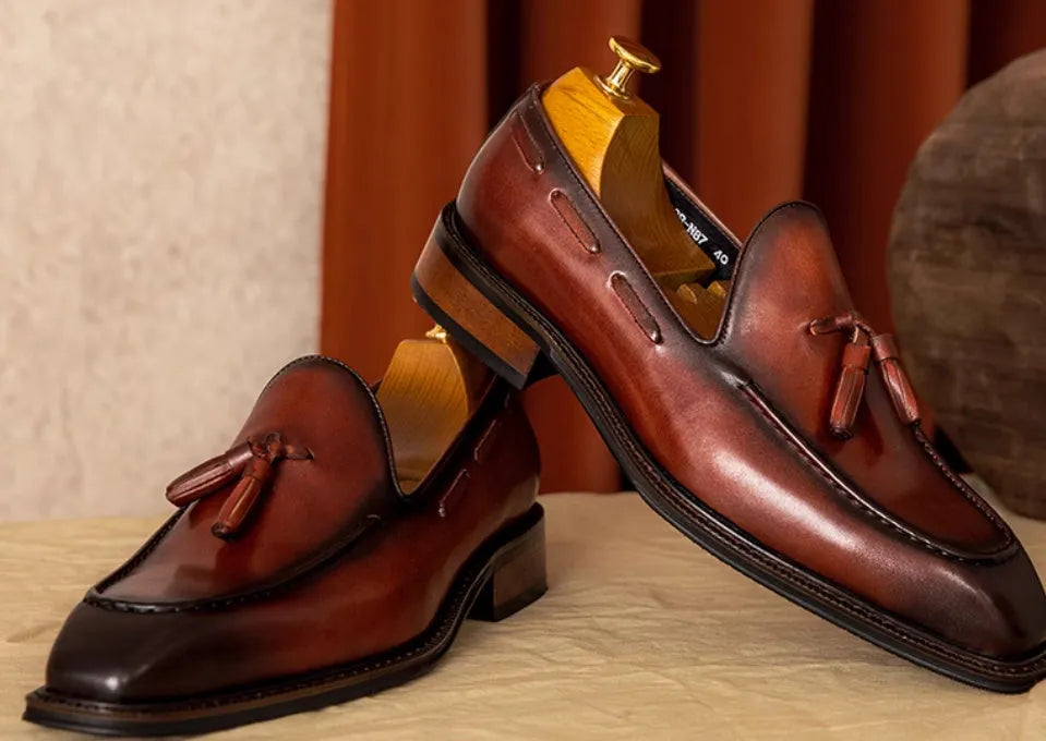 Men's black leather slip-on loafers with a fringed detail on the vamp and a rubber sole.