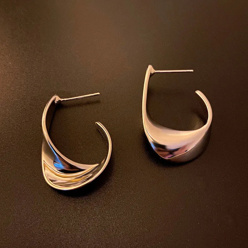 A pair of twisted geometric design metal earrings in a gold colour on a plain background