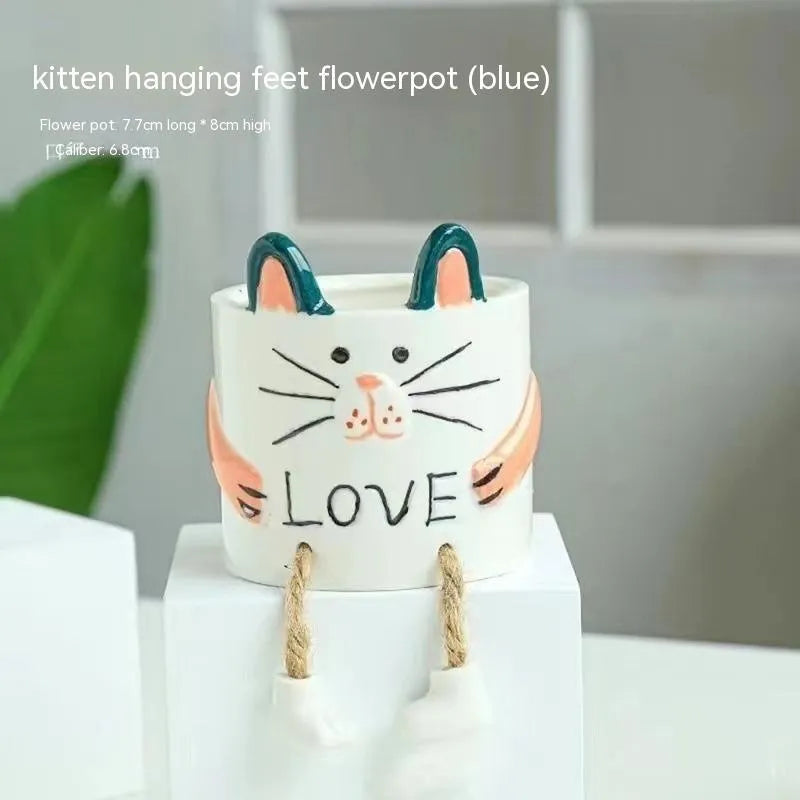 Ceramic hanging foot flowerpot in a cartoon style, shown on a desktop with a small succulent plant.
