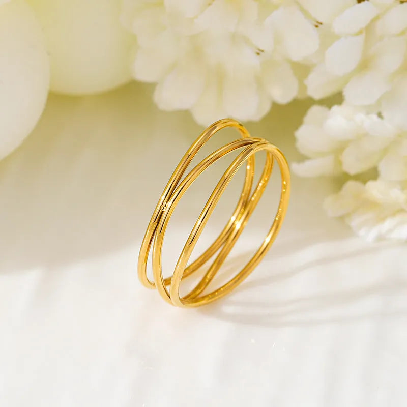 Gold geometric titanium steel coil ring showing three-layer bracelet-like design on a finger.