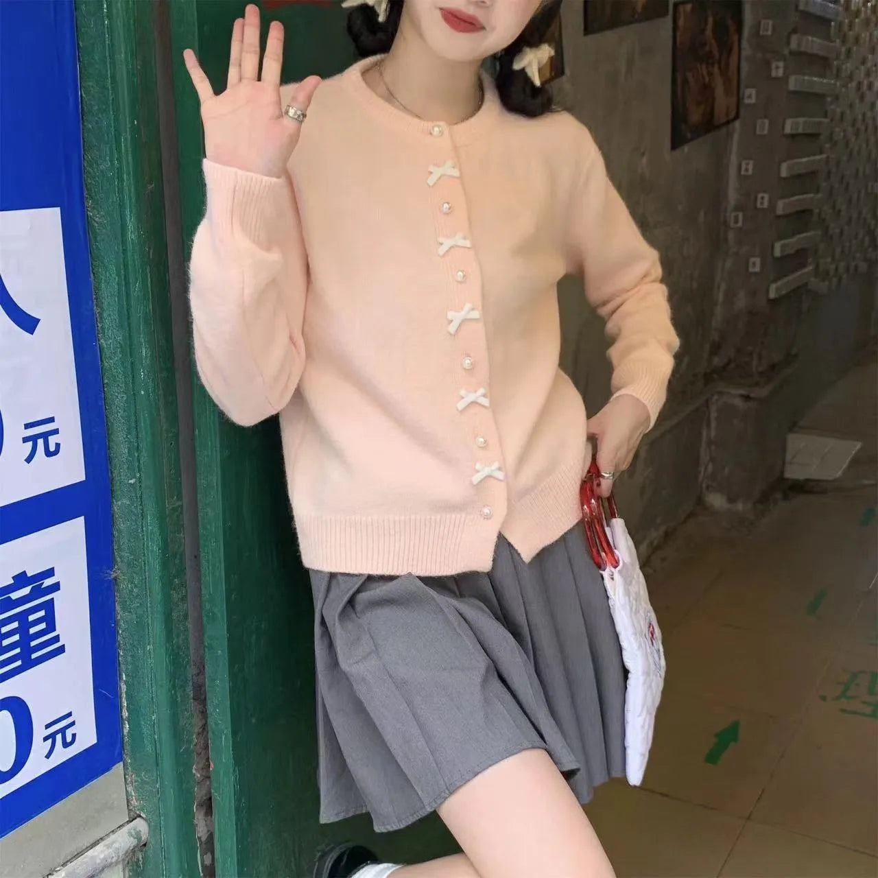 Women's light pink cardigan sweater with a black bow detail and pearl buttons on a hanger.