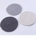 Three round grey cotton cord coasters placed on a wooden table, each 18cm in diameter.