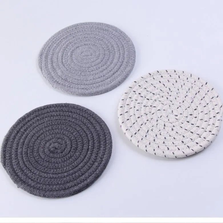 Three round grey cotton cord coasters placed on a wooden table, each 18cm in diameter.