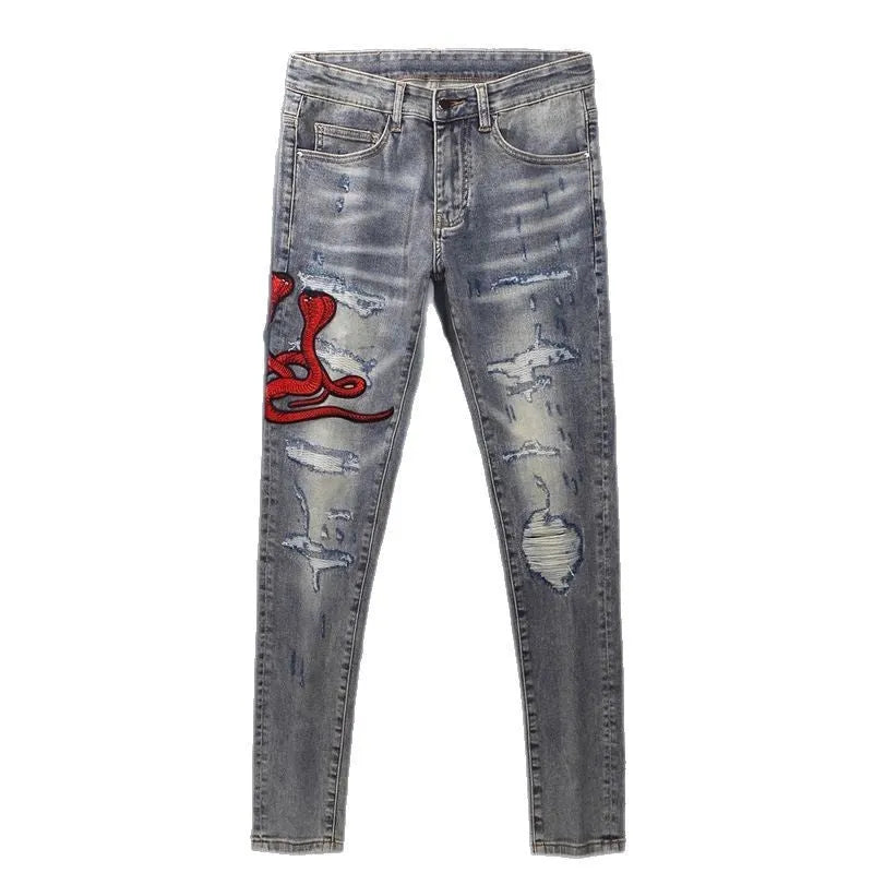 Slim-fit light blue jeans with a worn wash, knee holes, patch details, and embroidered branding on the leg.