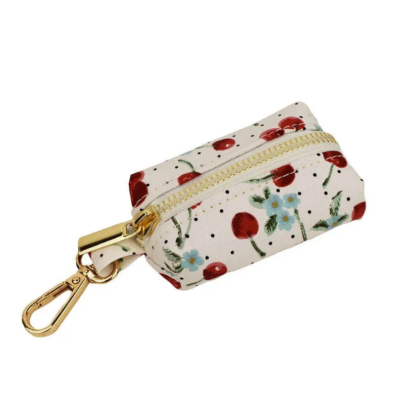 Red cherry printed cloth dog collar set with light gold buckle, matching leash, bow, vest, and bag.