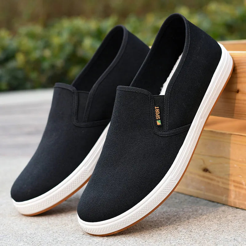 Men's black slip-on canvas trainers with round toe and low-top design on a white background