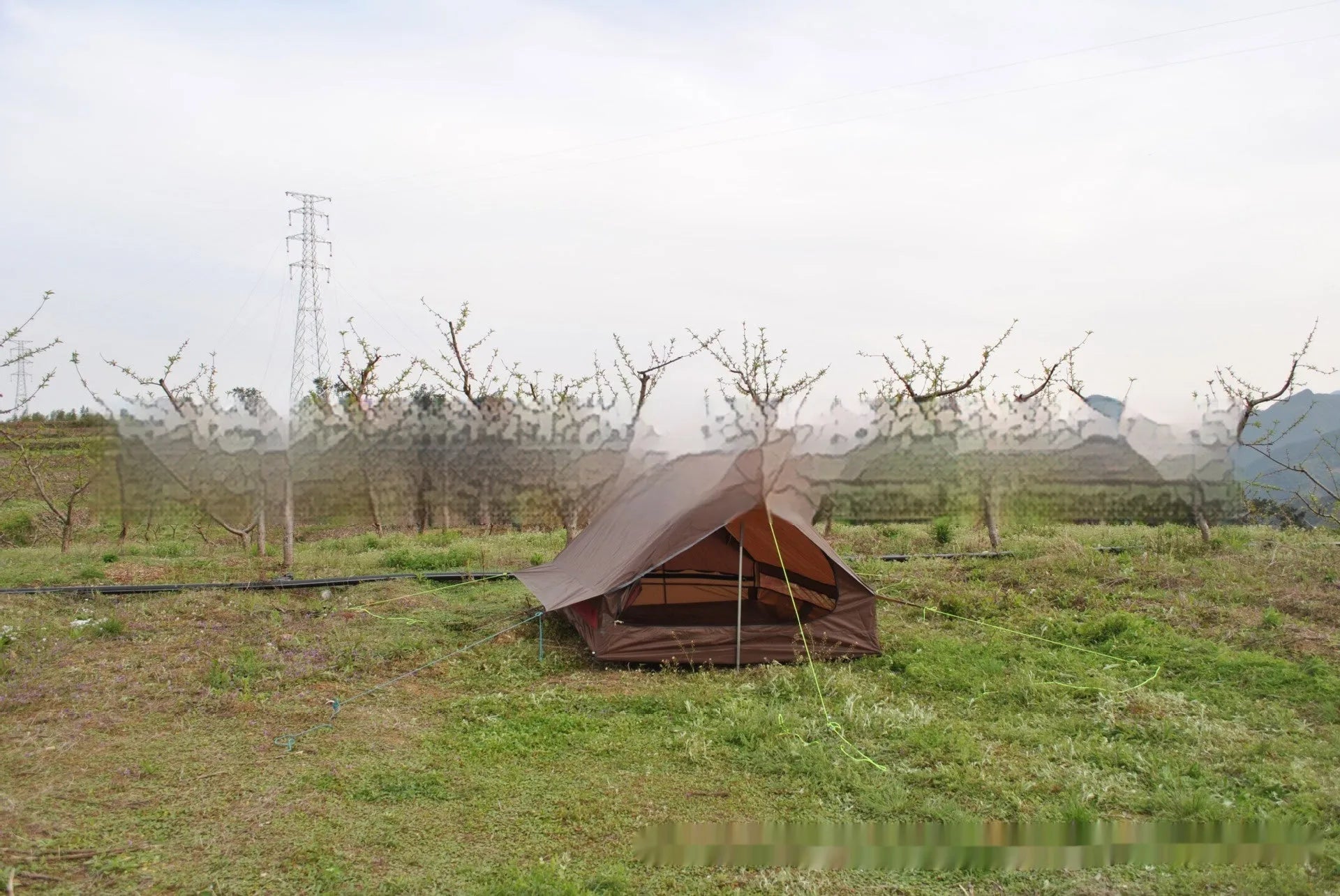 Brown A-line tent pitched with hiking poles, showing guy lines and aluminium ground nails.