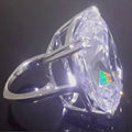 Simple white gold colour alloy ring with an inlaid square diamond, shown on a finger.