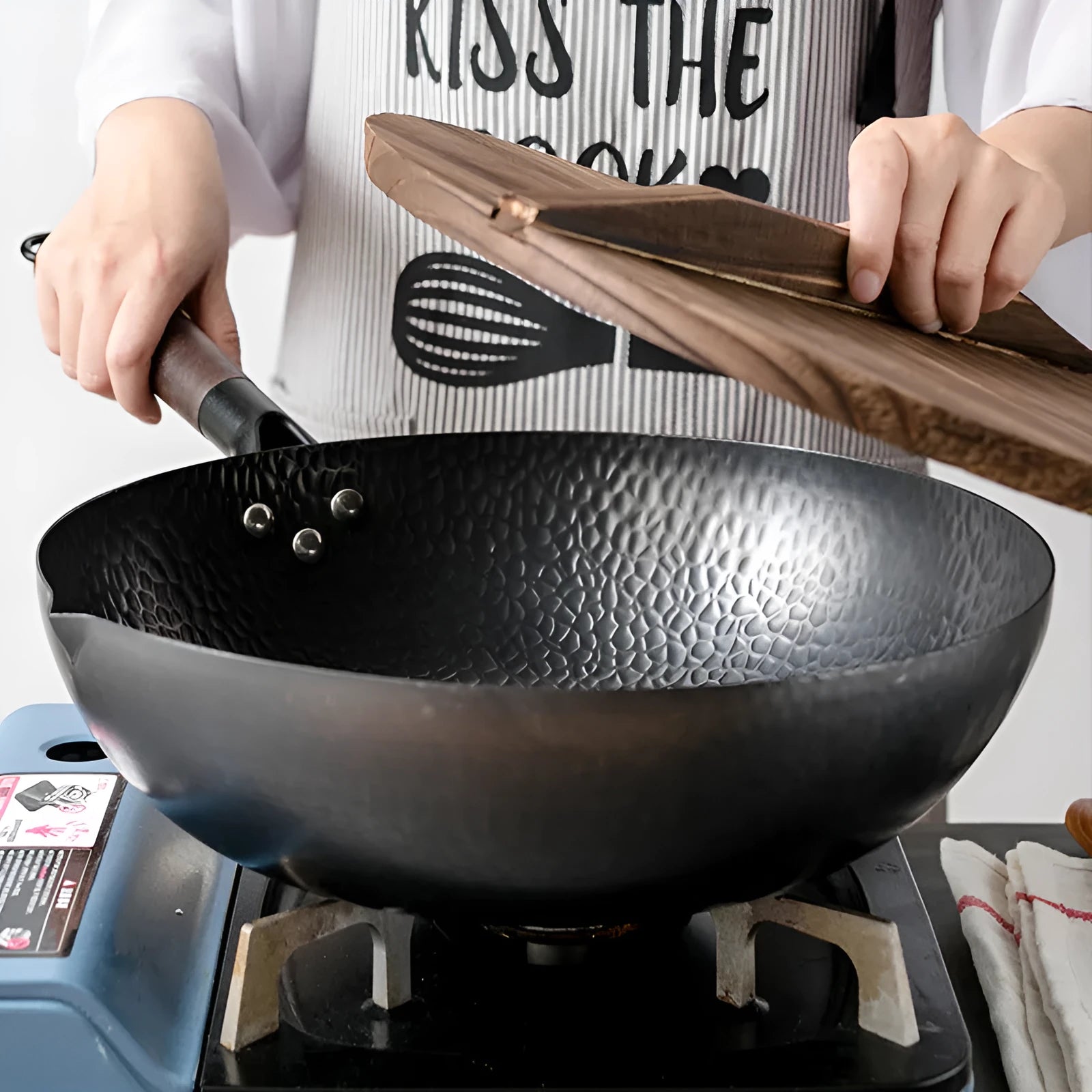 Black handmade traditional iron wok with a wooden handle on a stovetop.