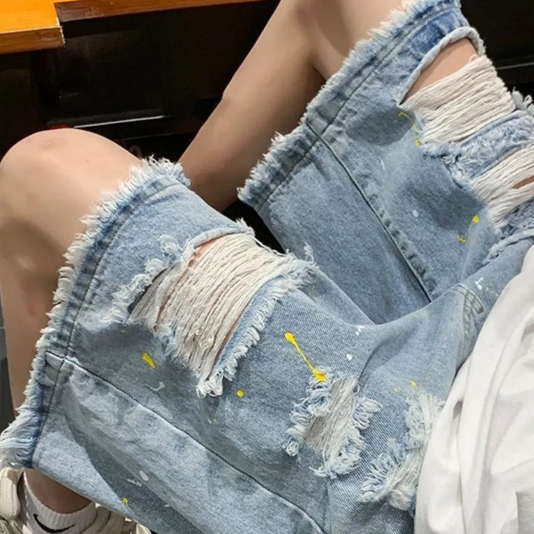 Man wearing loose light blue denim shorts with a distressed hole detail and water-washed finish.