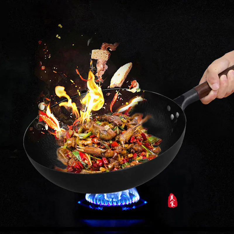 Black handmade traditional iron wok with a wooden handle on a stovetop.