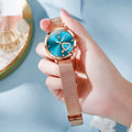 Women's fashion watch with rose shell detail, mesh strap, and choice of white, black, blue, red, pink, or green dial.
