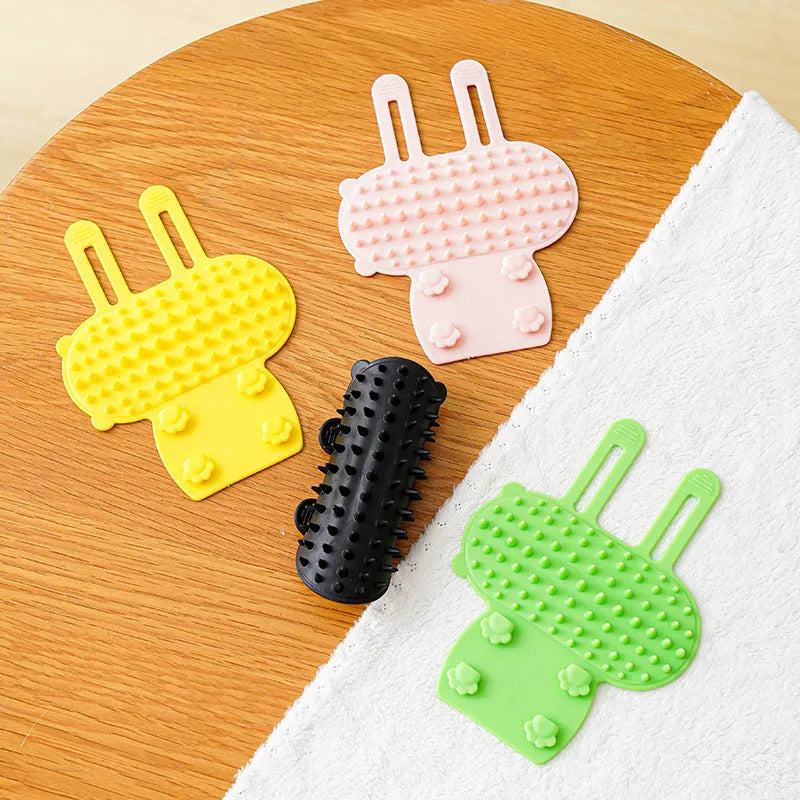 Silicone cat grooming massage comb with adjustable strap mounted on a table leg.