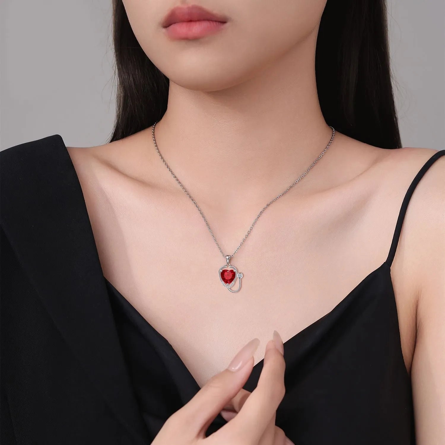 Red diamond stethoscope necklace with a wing and cross pendant on a chain.