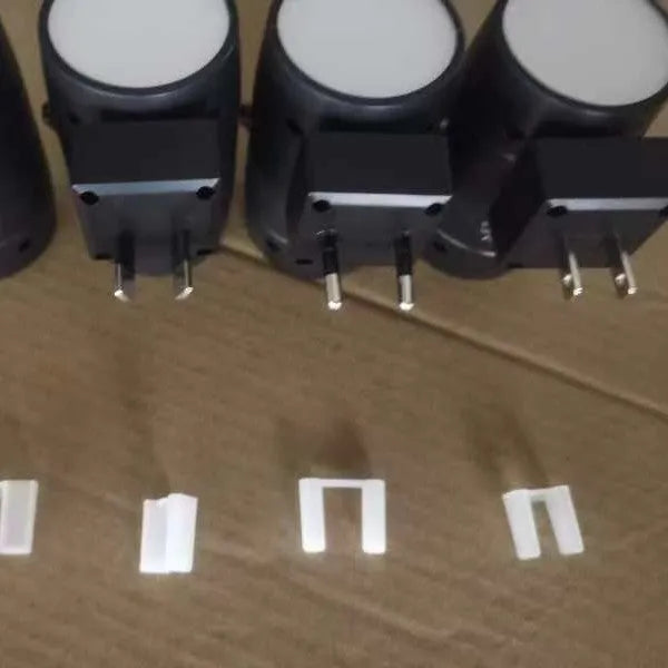 A small, white, direct plug-in night lamp with an adjustable and rotatable light head, shown plugged into a wall socket.