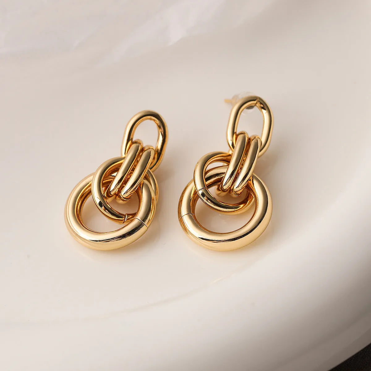 A pair of gold-coloured geometric earrings with an irregular shape on a white background.