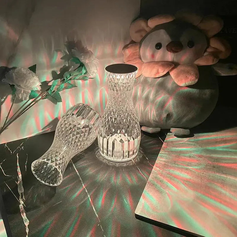 Transparent vase-shaped crystal LED table lamp on a table, showing soft coloured light.
