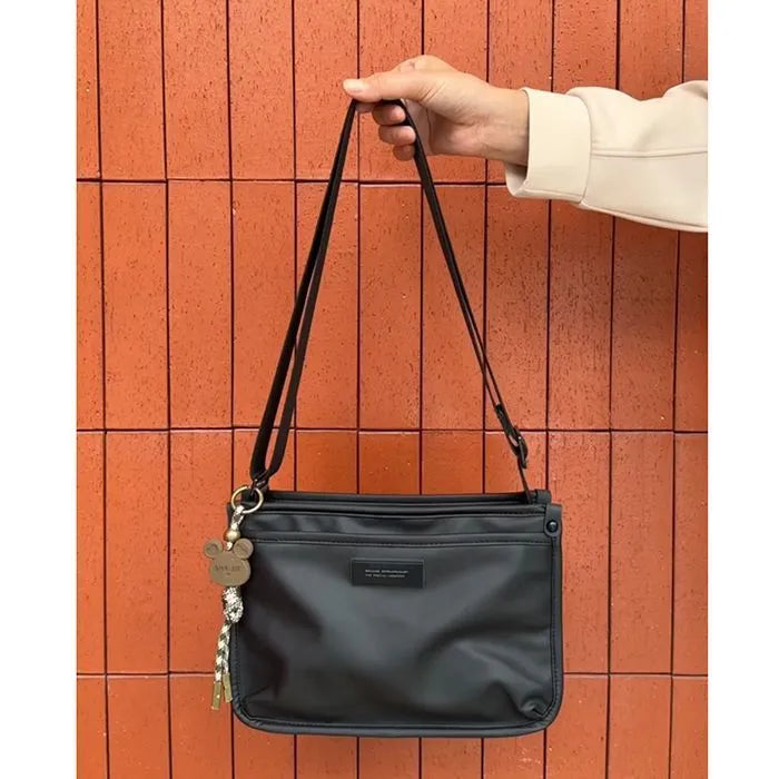 A small square crossbody bag in a cool retro style, made from textured Oxford cloth, shown on a person for scale.