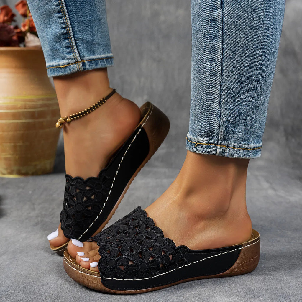 Women's black wedge beach slippers with floral cutouts on the PVC upper and a rubber sole.