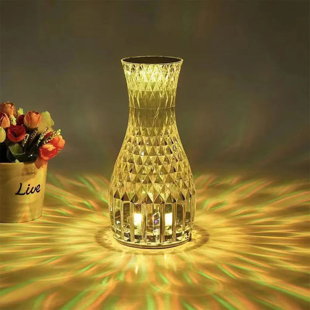 Transparent vase-shaped crystal LED table lamp on a table, showing soft coloured light.