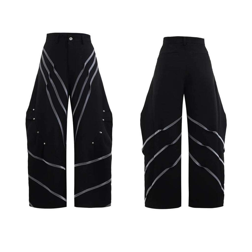 Men's black trousers with a deconstructing three-dimensional cut and pleats secured with metal striped rivets.