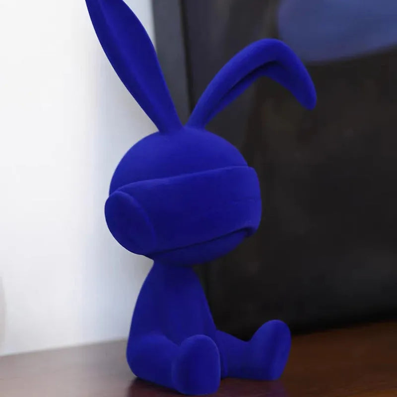 Green resin rabbit table ornament with a suede blindfold on a wooden shelf.
