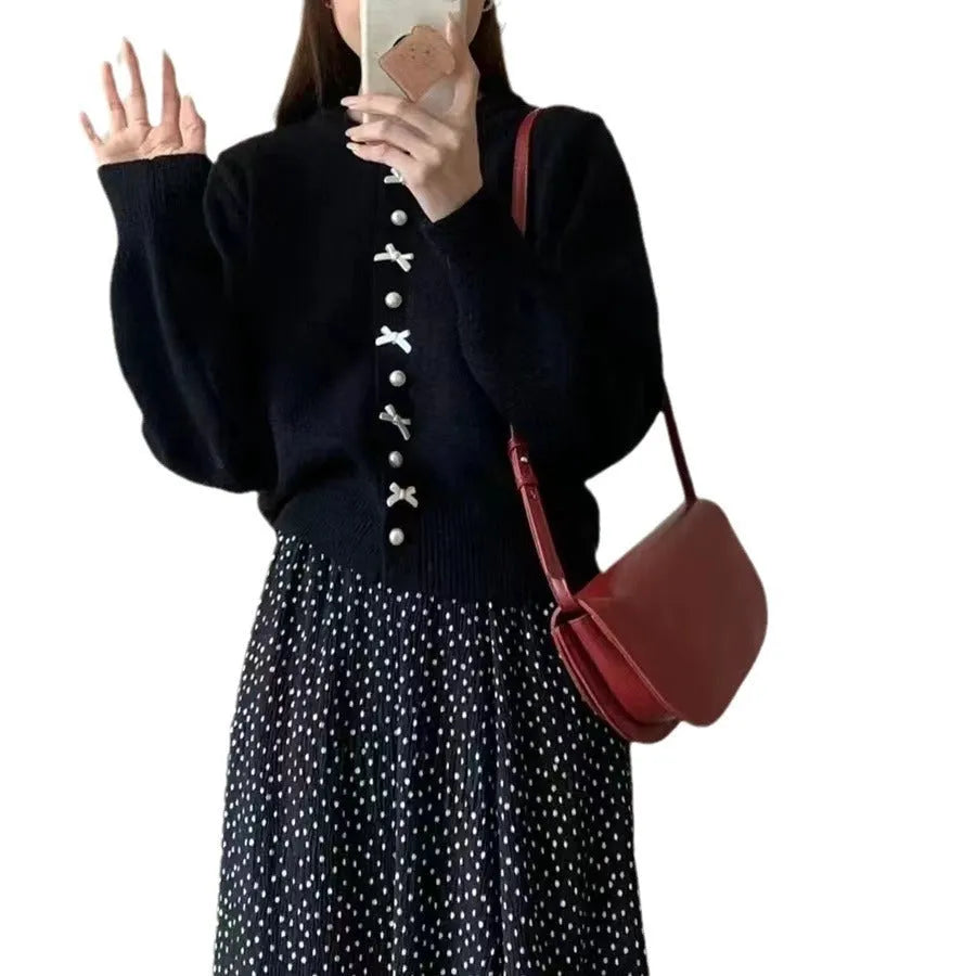 Women's light pink cardigan sweater with a black bow detail and pearl buttons on a hanger.
