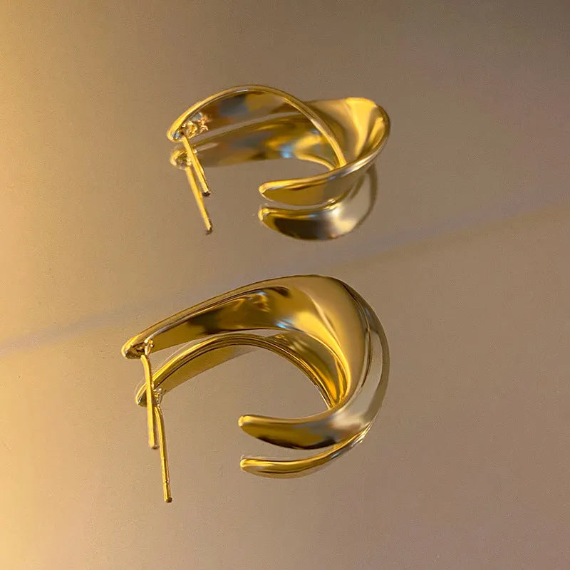 A pair of twisted geometric design metal earrings in a gold colour on a plain background