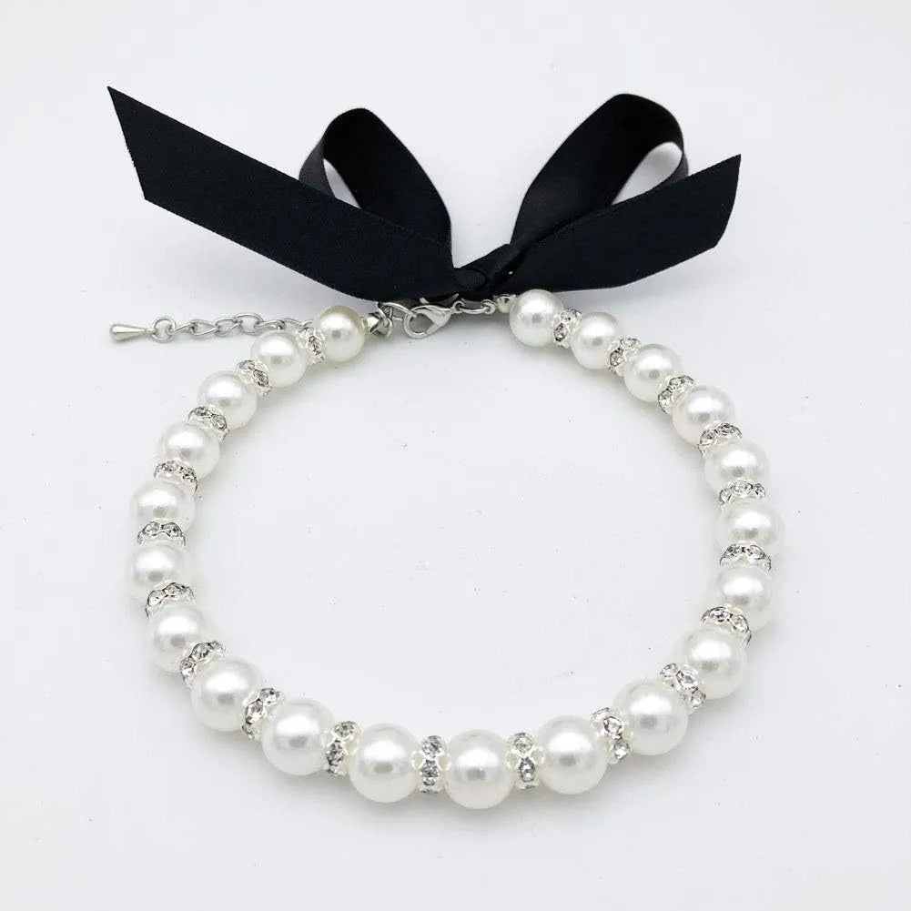 Small dog wearing a blue adjustable pearl and rhinestone necklace collar with a ribbon bow.