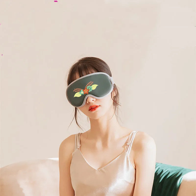 Pink portable eye spa massage goggles with USB cable on a grey background.
