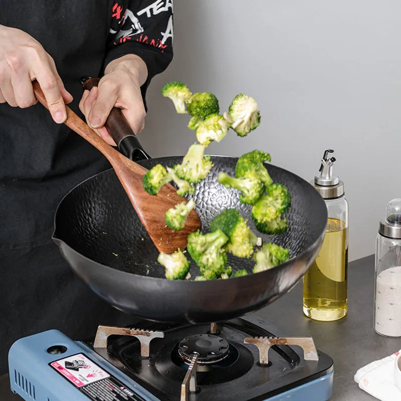 Black handmade traditional iron wok with a wooden handle on a stovetop.