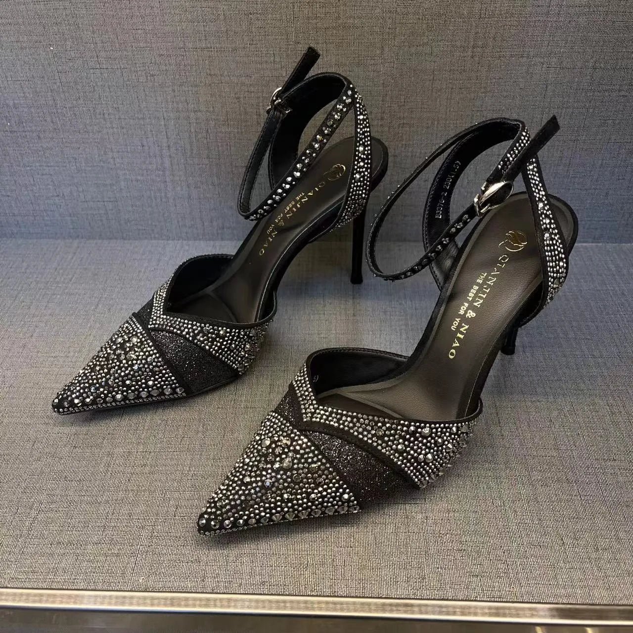 Women's black high heel shoe with a red sole, pointed toe, and a hollow stiletto heel on a plain background.