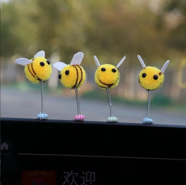 Small yellow and black fur ball bee car decoration on a plastic surface.