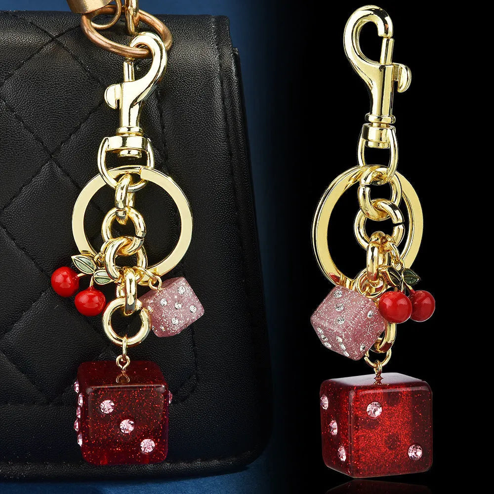 Close-up of a cherry red and white metal dice keychain pendant with a square pattern on a vintage-style suitcase charm.