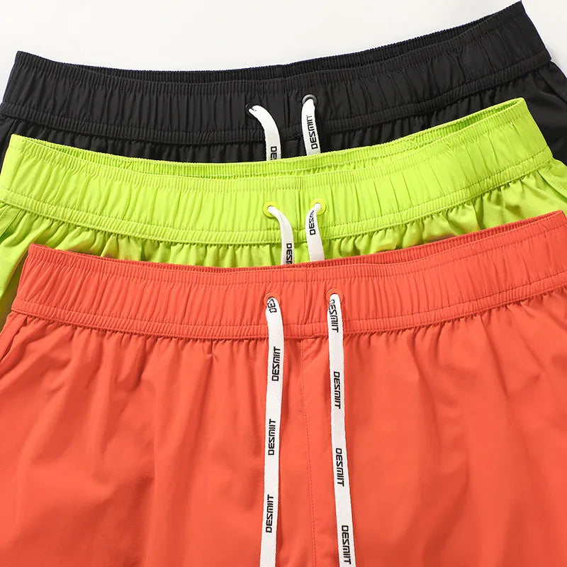 Men's loose elastic polyester shorts in orange, fluorescent green, and black colours for beach surfing.