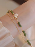 A green olivine stone bracelet with double layers, an Olive Branch charm, and Twin Bells of Ireland pendant.