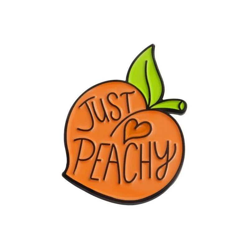 Colourful cartoon fruit design metal letter brooch on a fabric background.