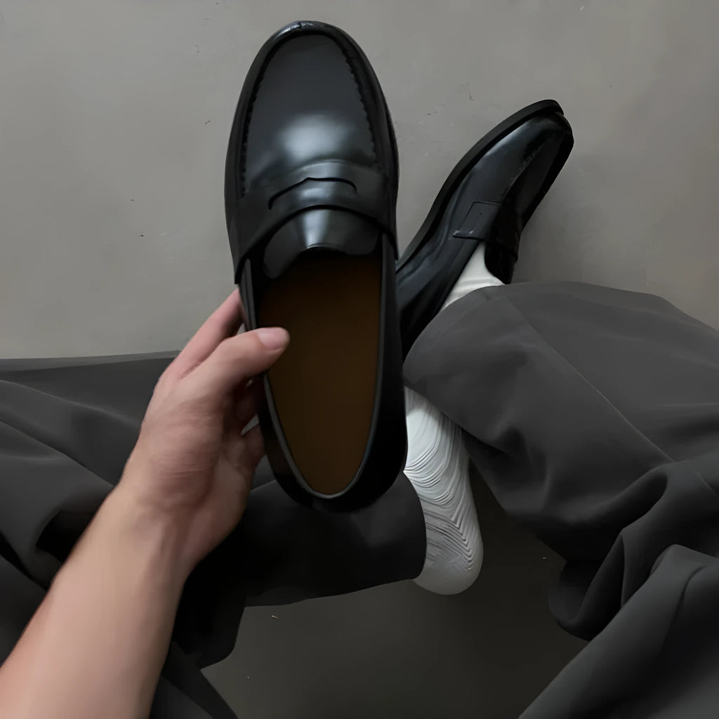 Men's black British-style slip-on leather loafers with stitched seams and vulcanised rubber sole on a plain background