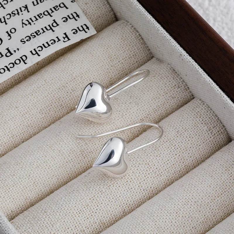 Pair of silver-tone 3D glossy heart-shaped drop earrings on a white background.