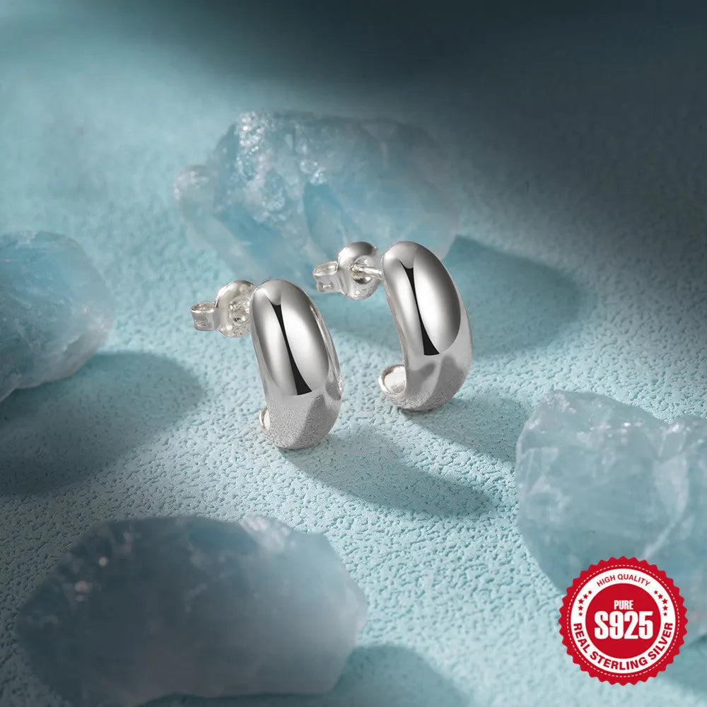 A single pair of glossy C-shaped sterling silver stud earrings on a white background.