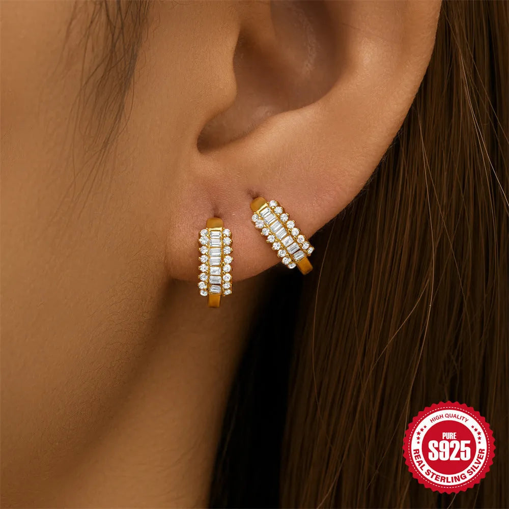 A pair of sterling silver stud earrings with a small round geometric drop design, shown in a gold tone finish.